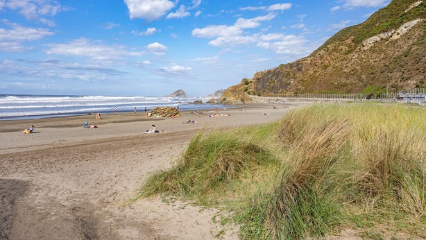 Una playa con orilla arenosa, dunas cubiertas de hierba y un acantilado rocoso.