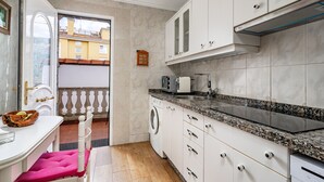 Cocina compacta con armarios blancos, encimera de granito, lavadora y vistas a través de una puerta abierta.