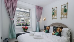 Un dormitorio con cama, cortinas, una ventana con vistas, una lámpara de pared y una planta decorativa.