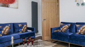 Una sala de estar con dos sofás azules, una puerta de madera, un radiador y un elemento decorativo en la pared.