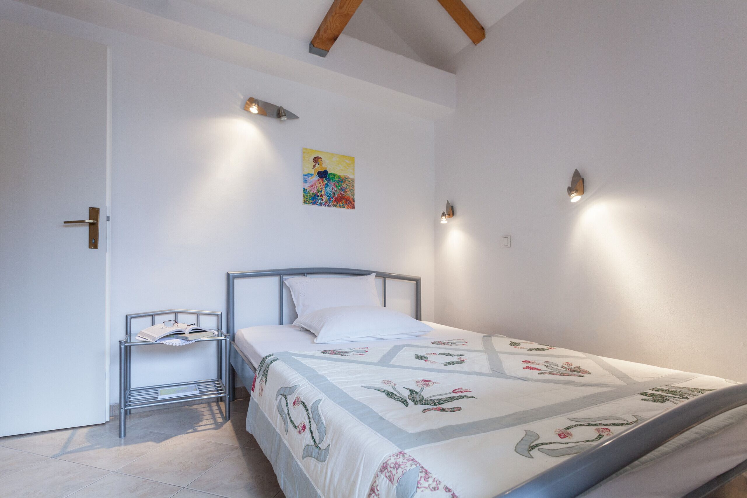 Ein Schlafzimmer mit Bett, Nachttisch, Wandregal und einem Gemälde.
