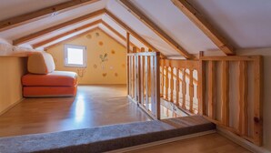 An attic bedroom with a wooden ceiling, a small window, and a wooden railing.