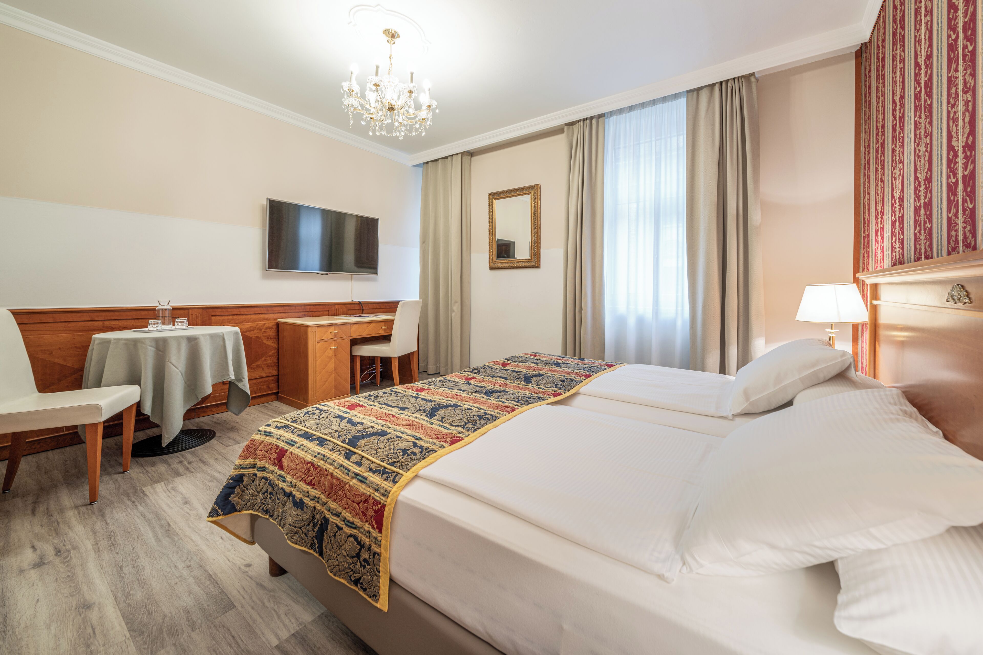 Ein Hotelzimmer mit einem großen Bett, einem Schreibtisch mit Stuhl, einem Fernseher und einer Chandelier.