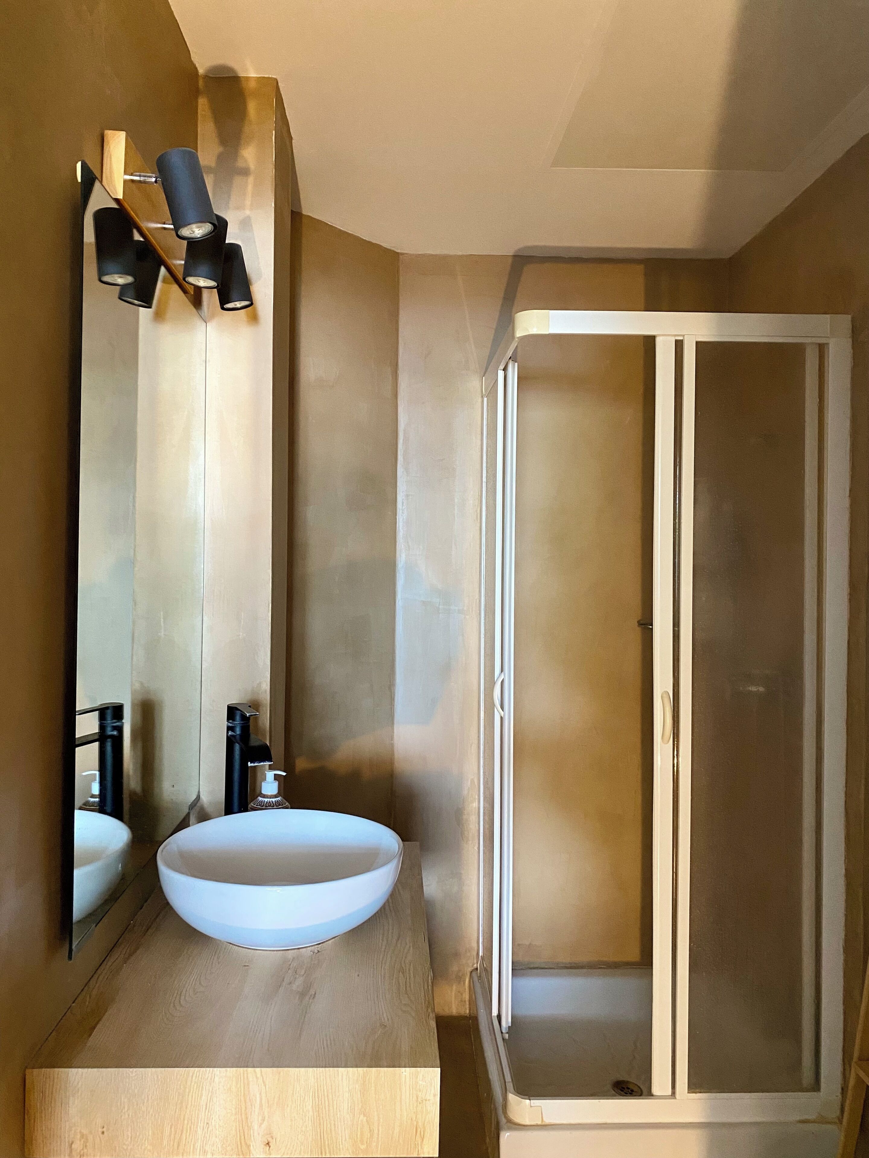 A bathroom with a wooden vanity, a white sink, a mirror, and a glass-enclosed shower.