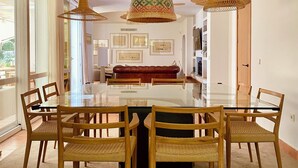 A dining area with a glass table surrounded by wicker chairs, wooden beams on the ceiling, and pendant lights. - Unique front line golf villa in Marbella (Marbella)