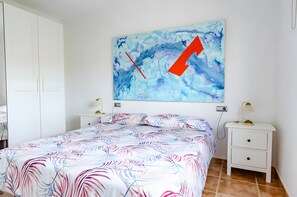 Un dormitorio con cama, mesitas de noche, un armario blanco y una pared con un cuadro abstracto azul.