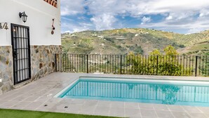 A swimming pool with a stone wall and a metal fence, set against a hillside with houses. - Villa 'Jema' with Sea Views, Private Pool and Air Conditioning (torrox)