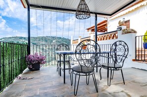 A balcony with a table and chairs, a potted plant, and a view of a hilly landscape.