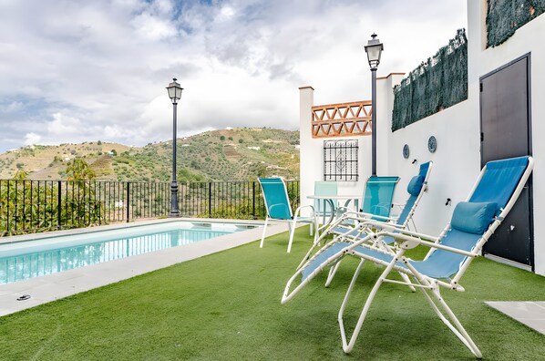 A pool area with artificial grass, a pool, and lounge chairs.