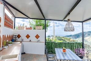Un espacio al aire libre cubierto con una mesa, sillas, plantas en macetas y vistas al campo.