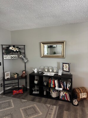 A room with a bookshelf, a decorative sign, a framed mirror, and a patterned rug.