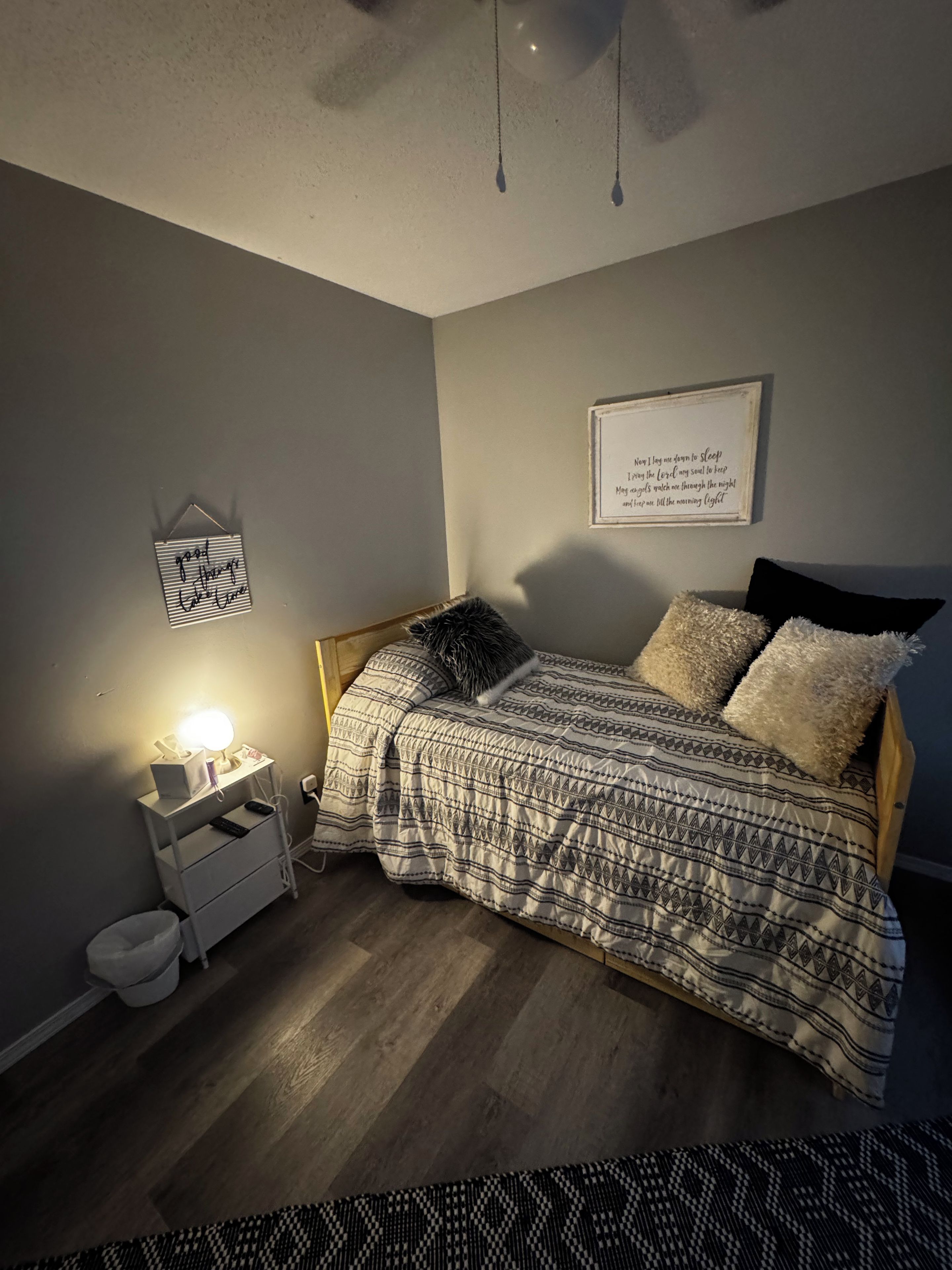 A bedroom with a bed, bedside table, lamp, and a framed quote on the wall.
