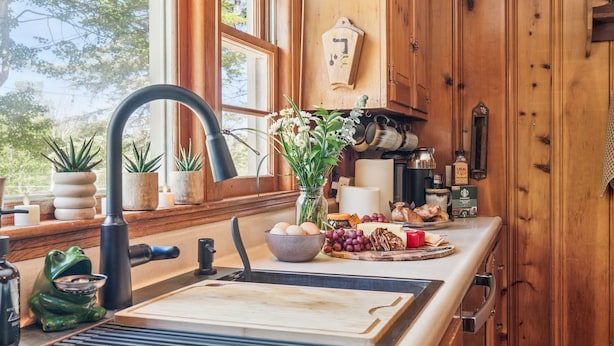 A rustic kitchen with wooden cabinets, a large window, and a variety of kitchen items on the counter.