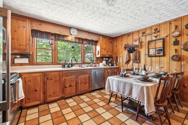Eine Küche mit Holzausstattung, gefliestem Boden, einem Esstisch für vier Personen und einem Fenster mit Blick auf Grünflächen.