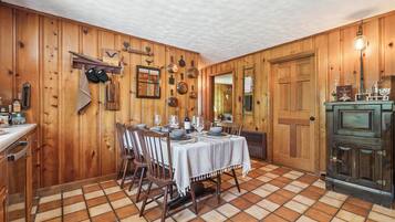 Comedor de madera con suelo de baldosas, una mesa dispuesta para cuatro comensales y un aparador de madera con espejo.