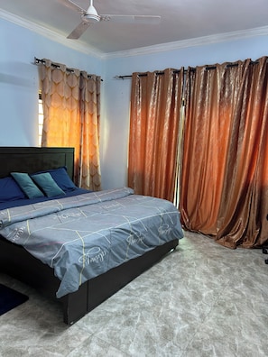 Een slaapkamer met een bed, gordijnen, een plafondventilator en een betegelde vloer.