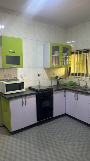 Een keuken met witte betegelde wanden, groene kastjes, een magnetron, een fornuis en een spoelbak.