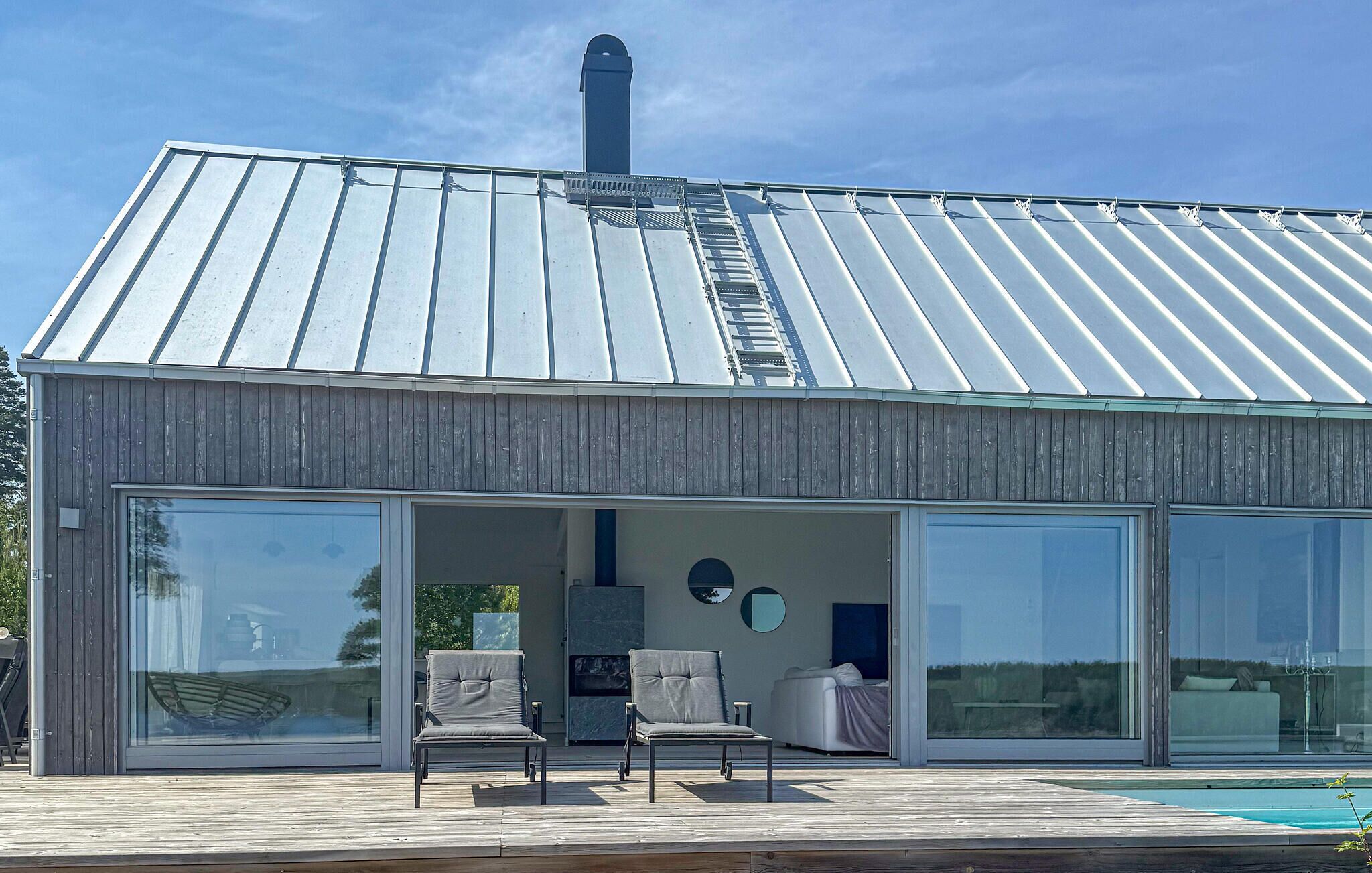 Une maison moderne avec un toit en métal, de grandes portes vitrées et une terrasse en bois.