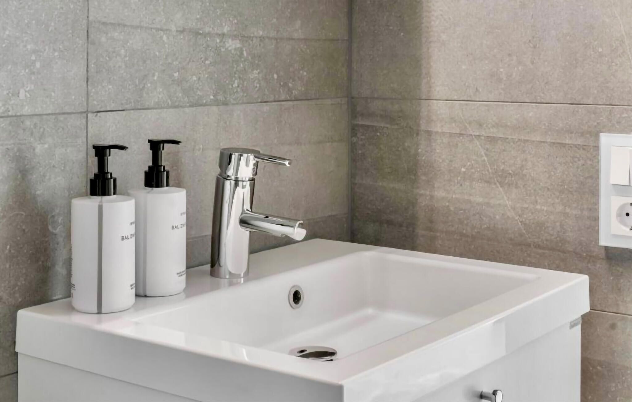 A bathroom with a white sink, chrome faucet, and two white bottles with black pumps.