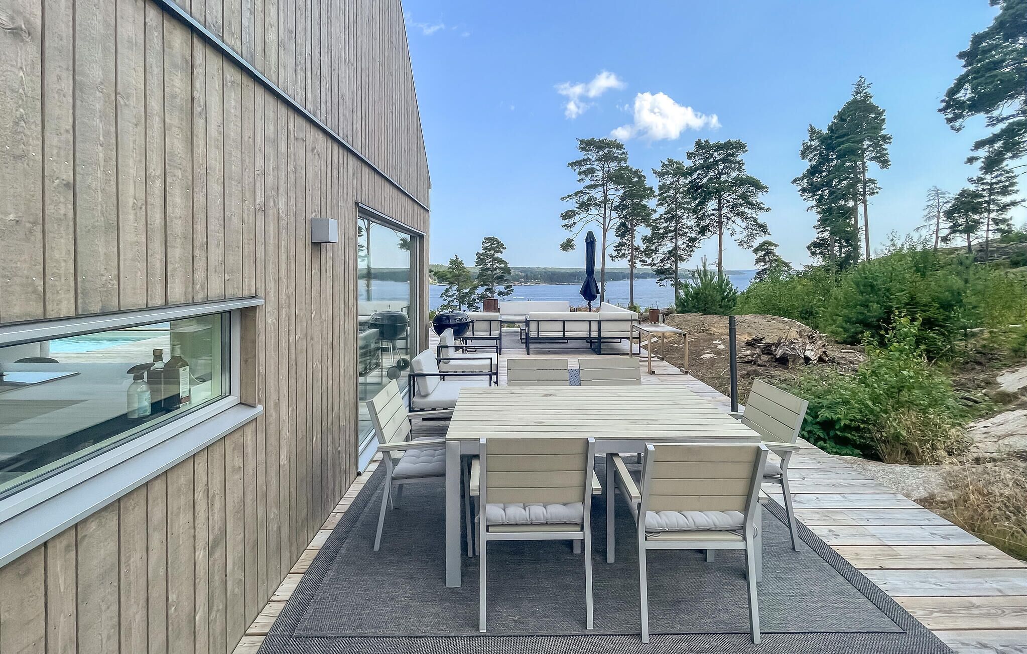 En träaltan med utomhusmöbler, en glasvägg och utsikt över havet.