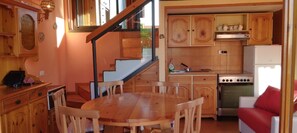 A kitchen with wooden cabinets, a dining table with chairs, a stove, and a refrigerator.