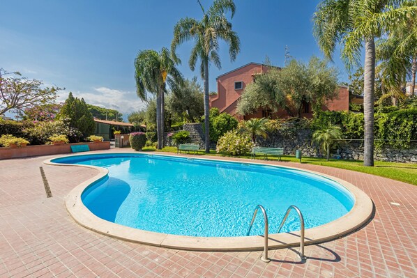 A swimming pool with a curved edge, surrounded by a brick patio.