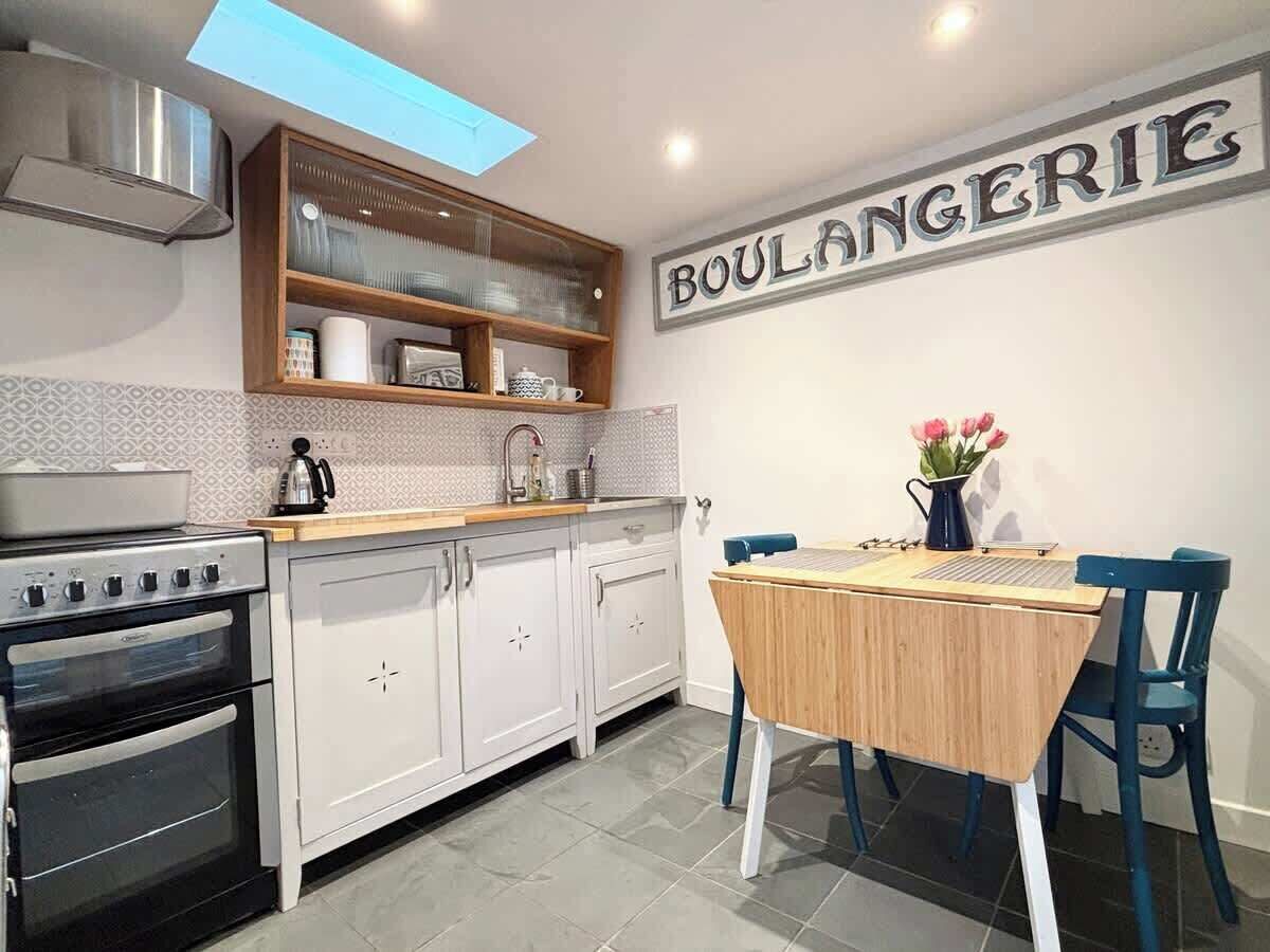 Une cuisine avec des meubles blancs, un plan de travail en bois, une cuisinière et une table à manger avec des chaises.