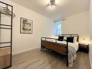 A bedroom with a bed, a nightstand, a window, a wall-mounted shelf, and a poster.
