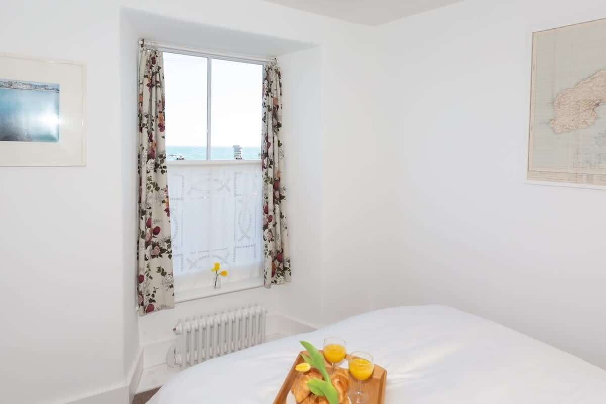 A bedroom with a bed, a window with floral curtains, a radiator, and a breakfast tray on the bed.
