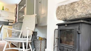 A cozy room with a rocking chair, a stone fireplace, and a kitchen area with cabinets and a toaster. - Janies Cottage- Eclectic Interiors & Vintage charm (Mousehole)