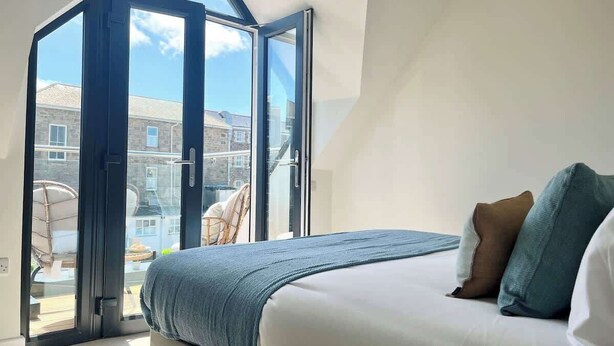 A bedroom with a large bed, a view through a glass door, and a balcony with a chair. - Kerensa, 3 bed with parking,  close to the beach (Penzance)
