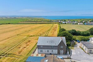 A rural landscape with a large building, open fields, and a distant view of the sea.