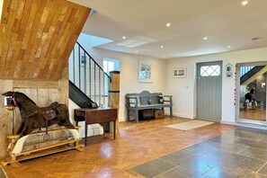 A spacious living area with a wooden horse sculpture, a piano, and a staircase leading to an upper level.
