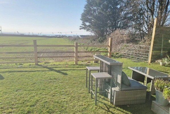 A grassy outdoor area with a wooden fence, wicker furniture, and a view of a field.
