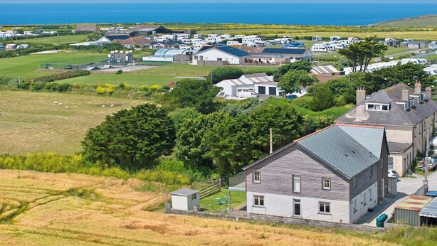 Un quartier résidentiel situé sur la côte, avec des maisons, un champ d’herbe et une vue sur la mer.