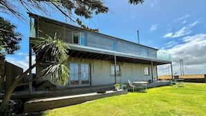 Une maison à deux étages avec un porche couvert, une pelouse et du mobilier d’extérieur.