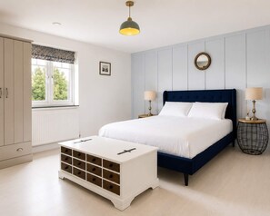 A bedroom with a bed, bedside tables, a dresser, a window, and a hanging light fixture.