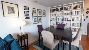 Un comedor con una mesa de madera oscura, cuatro sillas, una estantería y un cuadro enmarcado en la pared.