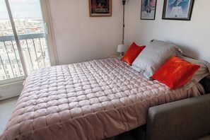 Un dormitorio con una cama grande, una mesita de noche, una lámpara y vistas de la ciudad a través de una ventana.