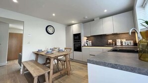 Una cocina moderna con armarios blancos, una mesa de comedor de madera y un reloj en la pared.