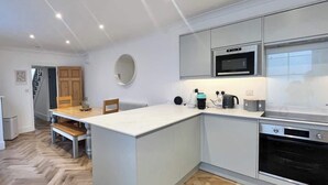Une cuisine moderne dotée d’un îlot central, d’appareils électroménagers intégrés et d’un parquet en bois disposé en chevrons.