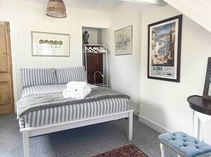 A bedroom with a bed, a bench, a coat rack, and framed pictures on the wall. - Charming 2-Bed Artist's Residence Central Penzance (Penzance)