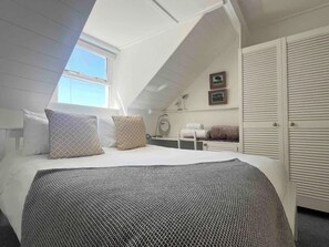 Un dormitorio con techo inclinado, una cama con ropa de cama estampada, una mesita de noche, un espejo y un armario.