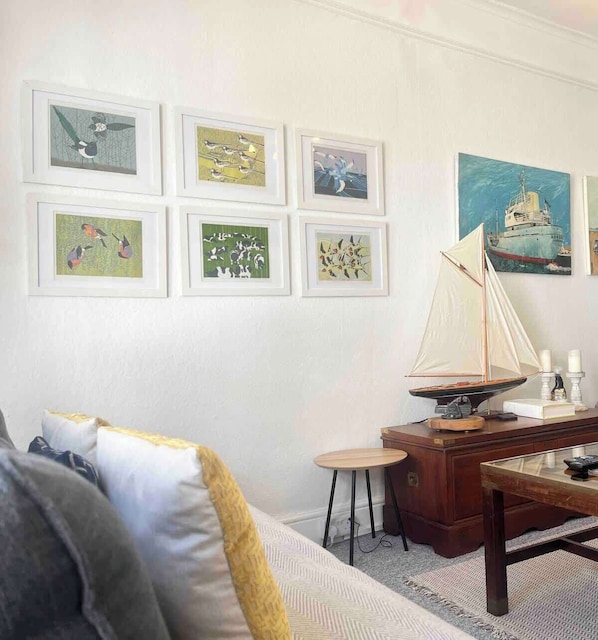 Ein Zimmer mit einem Bett, einem Schreibtisch, einem kleinen Tisch und einem Modell eines Segelboots. An der Wand hängen sechs gerahmte Kunstwerke.