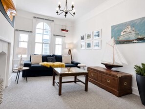 A living room with a dark sofa, a wooden coffee table, a sideboard, and a sailboat model. - Charming 2-Bed Artist's Residence Central Penzance (Penzance)