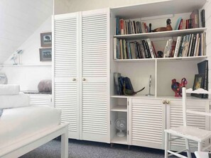 Ein Zimmer mit einem weißen Wandschrank, einem Bücherregal, einem weißen Sessel und einem kleinen Tisch.