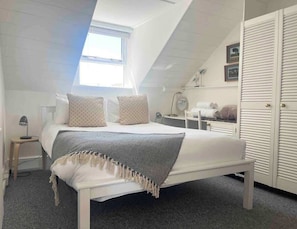 Ein Schlafzimmer mit Bett, Nachttisch, Lampe und Fenster.