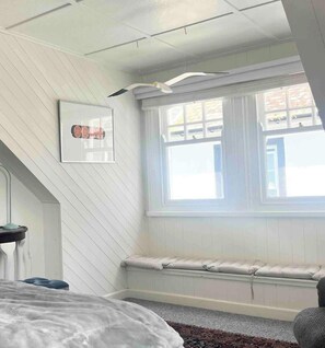 A bedroom with a large window, a bed, a bench, and a ceiling fan. - Charming 2-Bed Artist's Residence Central Penzance (Penzance)