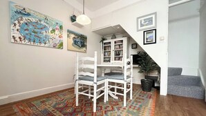 A spacious living room with a white dining table and chairs, a colorful rug, and a staircase leading to another level. - Charming 2-Bed Artist's Residence Central Penzance (Penzance)