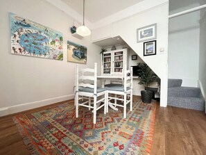Amplia sala de estar con una mesa de comedor blanca y sillas, una alfombra colorida y una escalera que conduce a otro nivel.